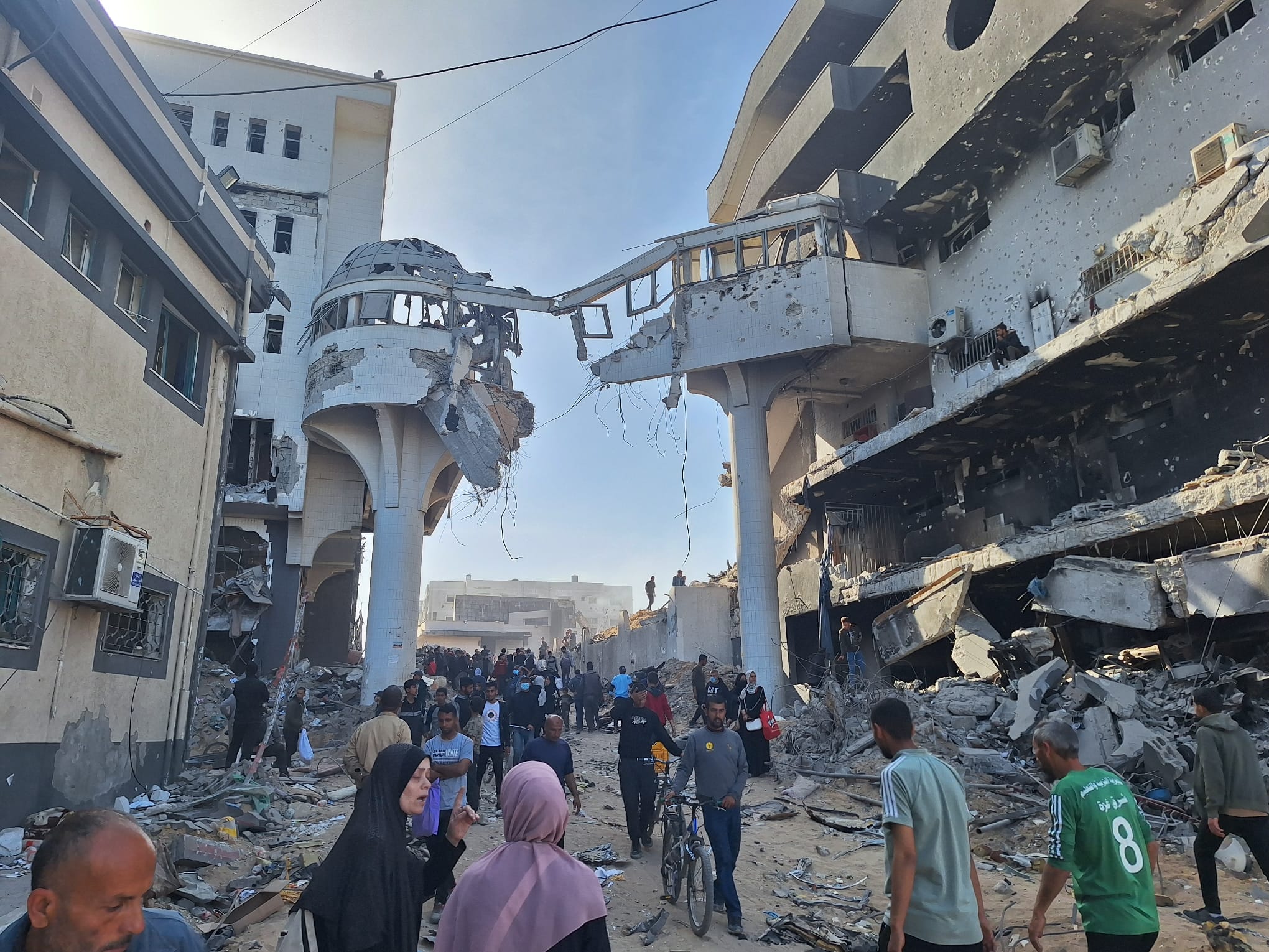 Gaza hospital under siege with Israeli forces outside, civilians awaiting medical aid amidst conflict.